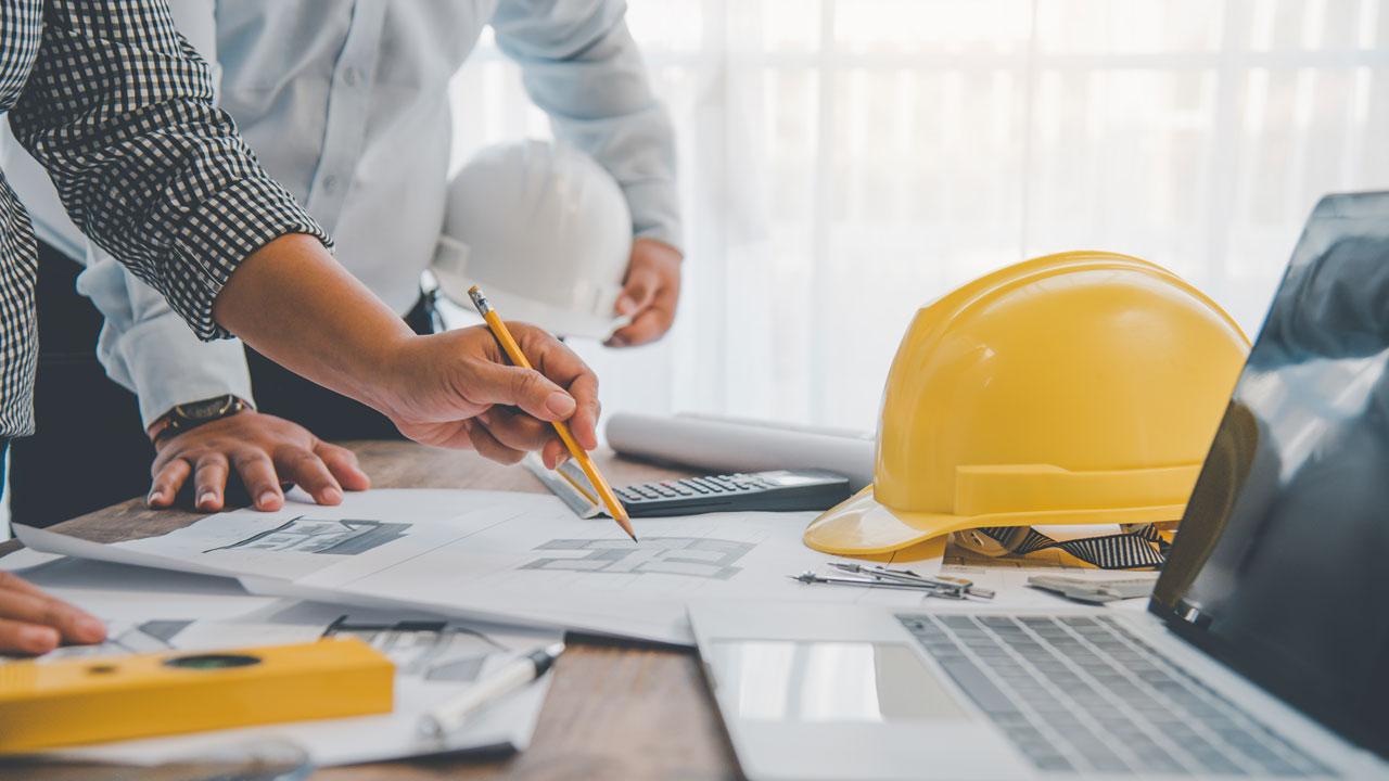 An open laptop, yellow hard hat, 在桌子上全球最大体育平台文件，全球最大体育平台们聚在一起审阅文件